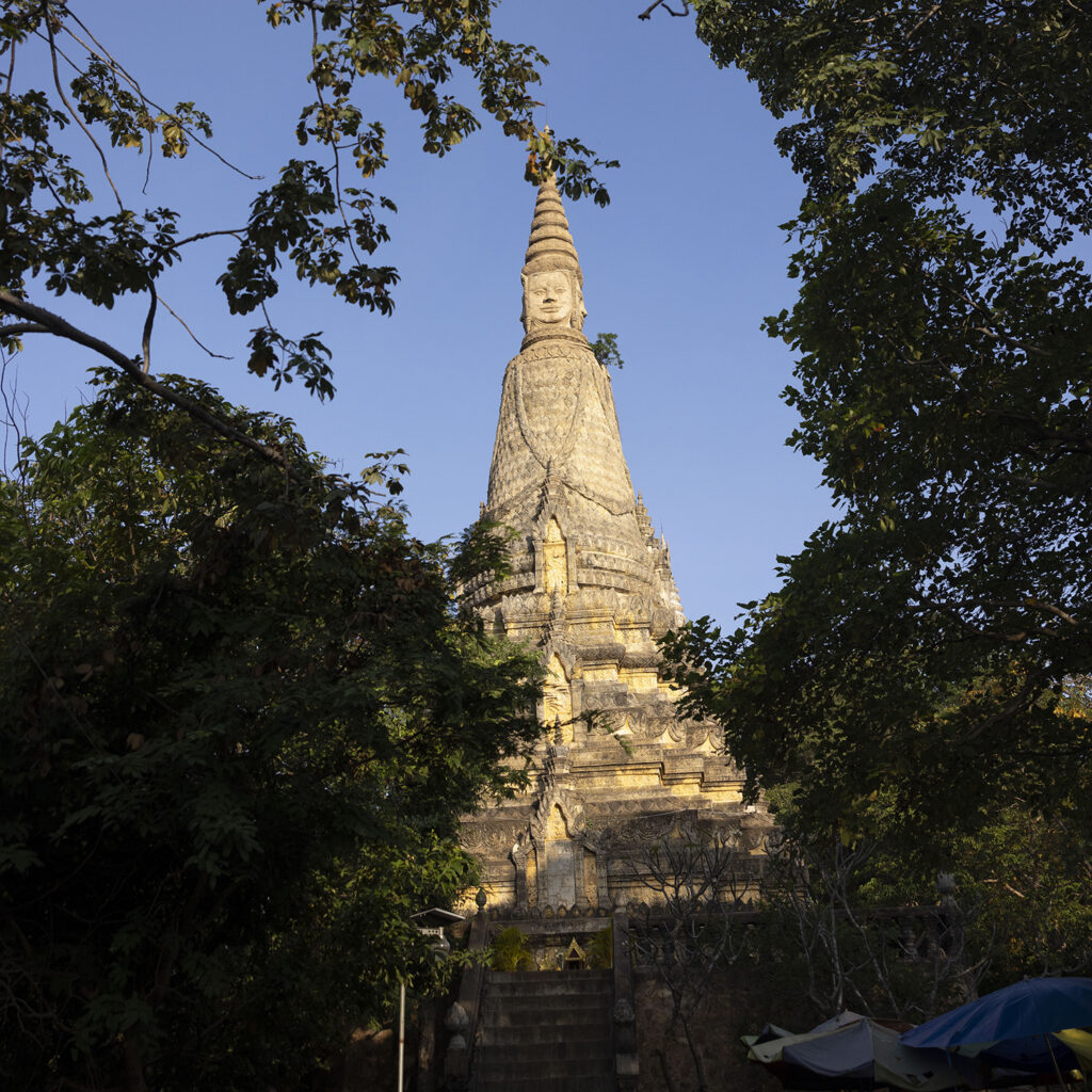 Stone Buddhist stupa rising above surrounding trees against a clear blue sky